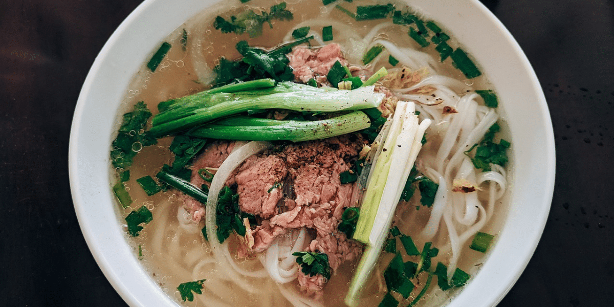 Bowl of chicken noodles soup with chunks of chicken, vegetables, and egg noodles, garnished with parsley on a wooden table