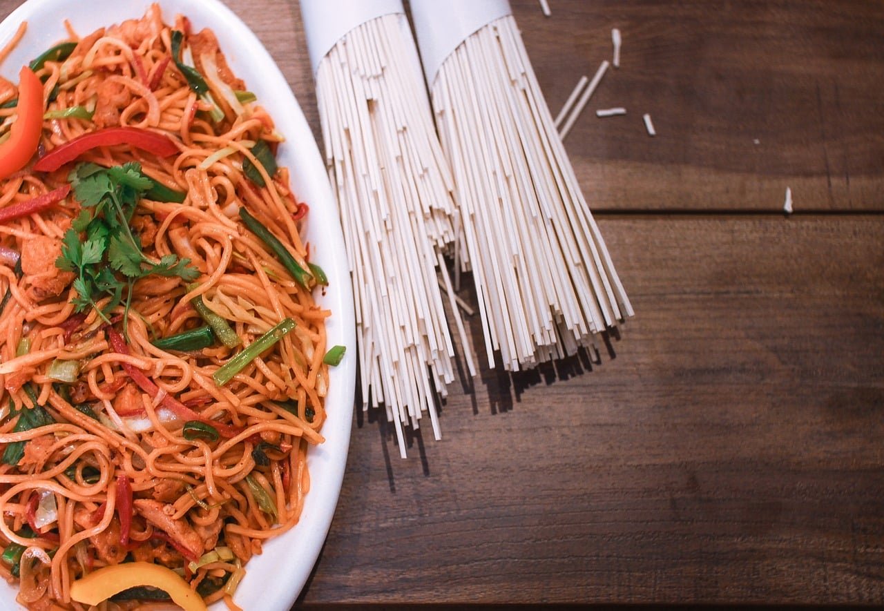 Bowl of chicken noodles soup with chunks of chicken, vegetables, and egg noodles, garnished with parsley on a wooden table.