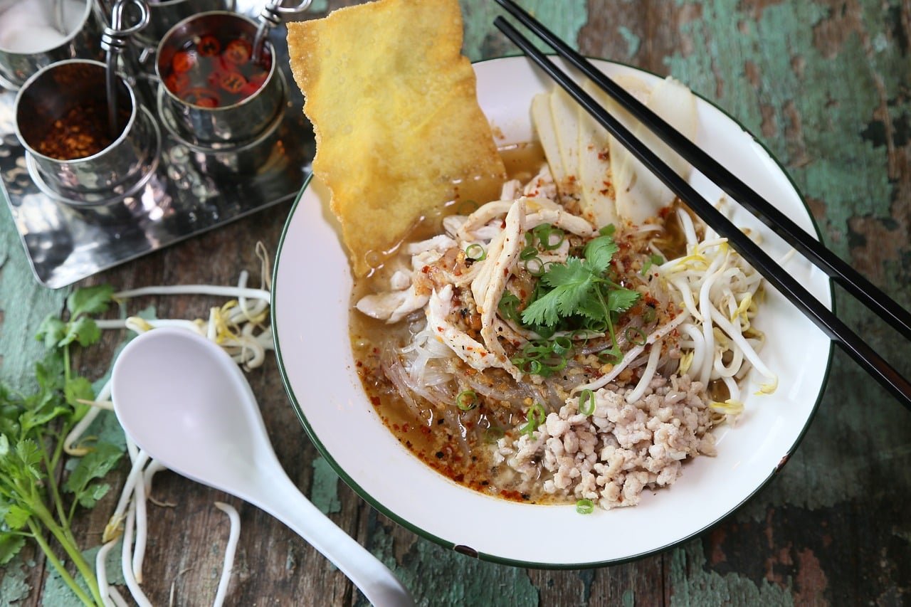 Bowl of chicken noodles soup with chunks of chicken, vegetables, and egg noodles, garnished with parsley on a wooden table.